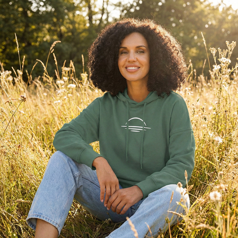 A woman sat in a sunny field wearing an organic cotton hoodie.