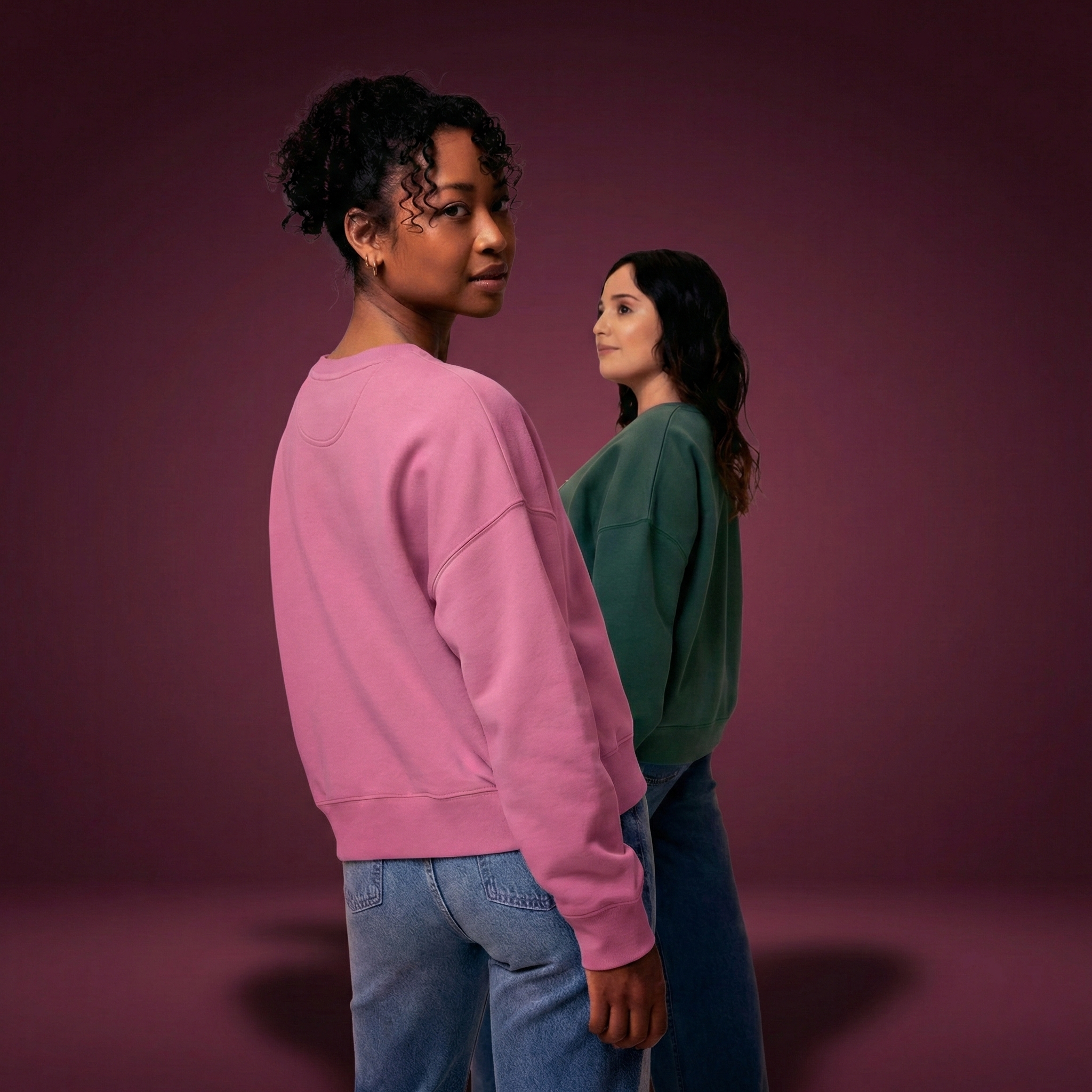 Two women wearing organic cotton sweatshirt jumpers in green and pink.